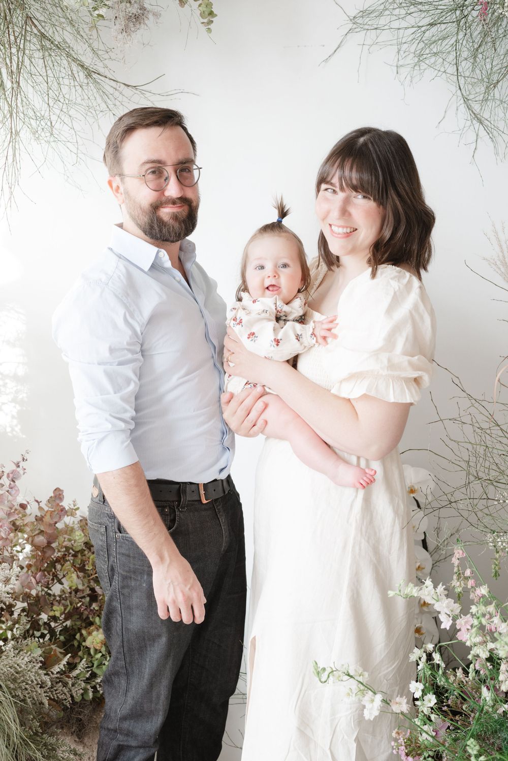Mother holding baby next to dad in floral Mother's Day setup at a family photoshoot in Toronto captured by Toronto Family Photographer
