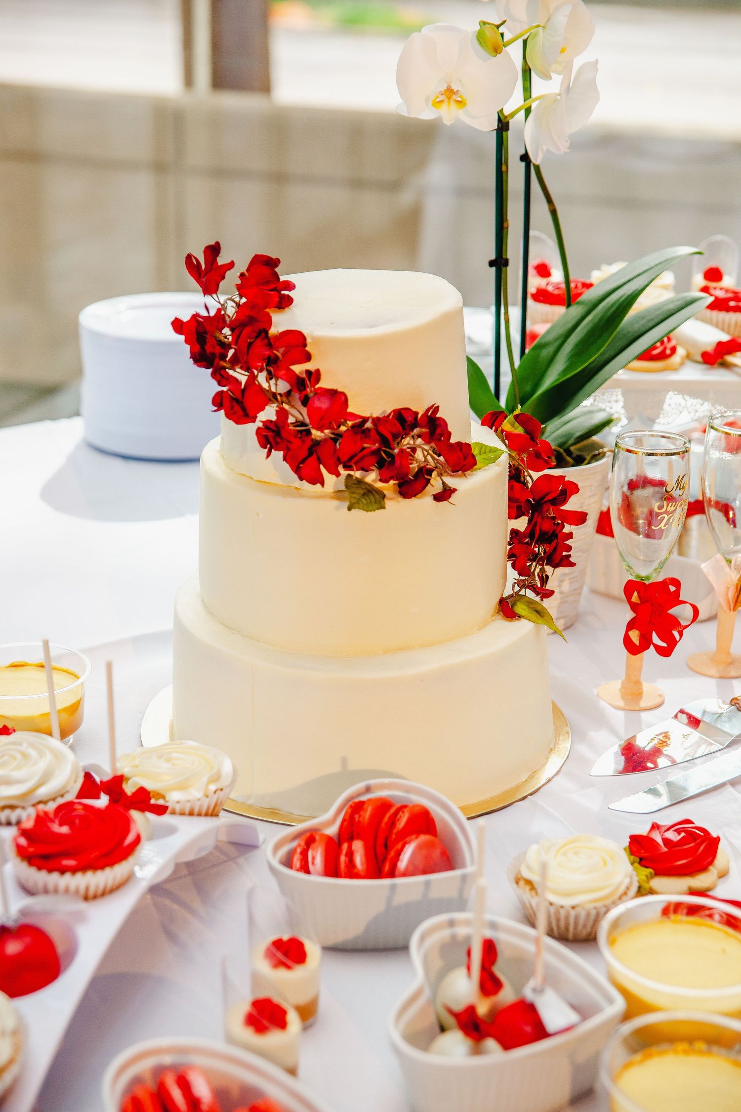 Elegant white wedding cake decorated with red orchids and tropical greenery.