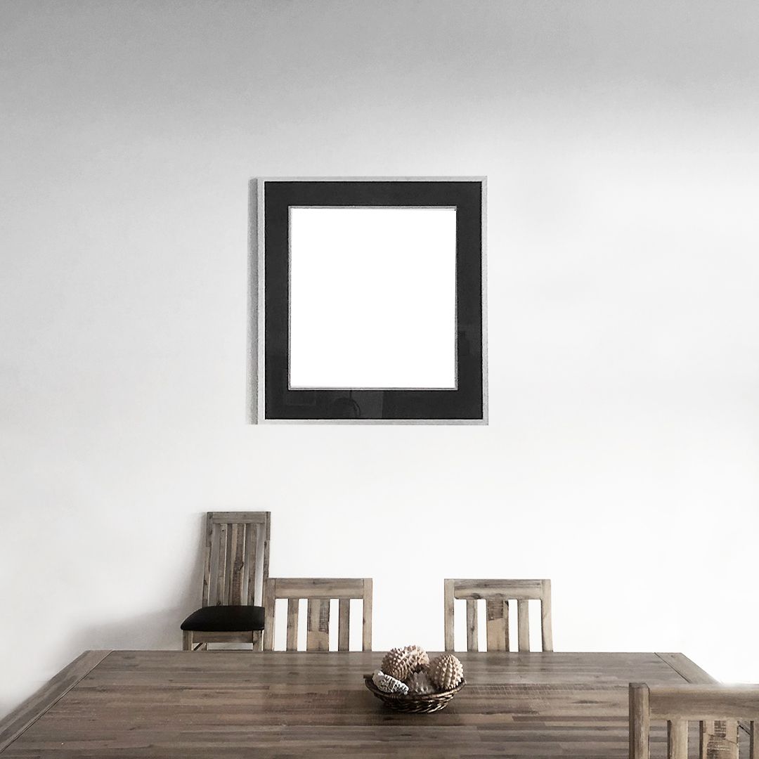 Modern dining space with blank black square frame on white wall above wooden furniture.