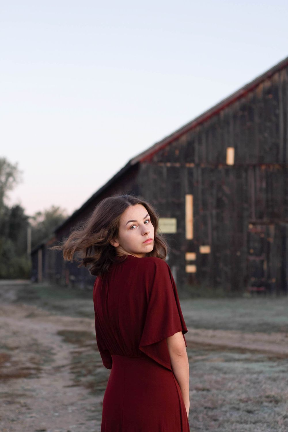 High school senior flipping her hair in front of a barn at sunrise