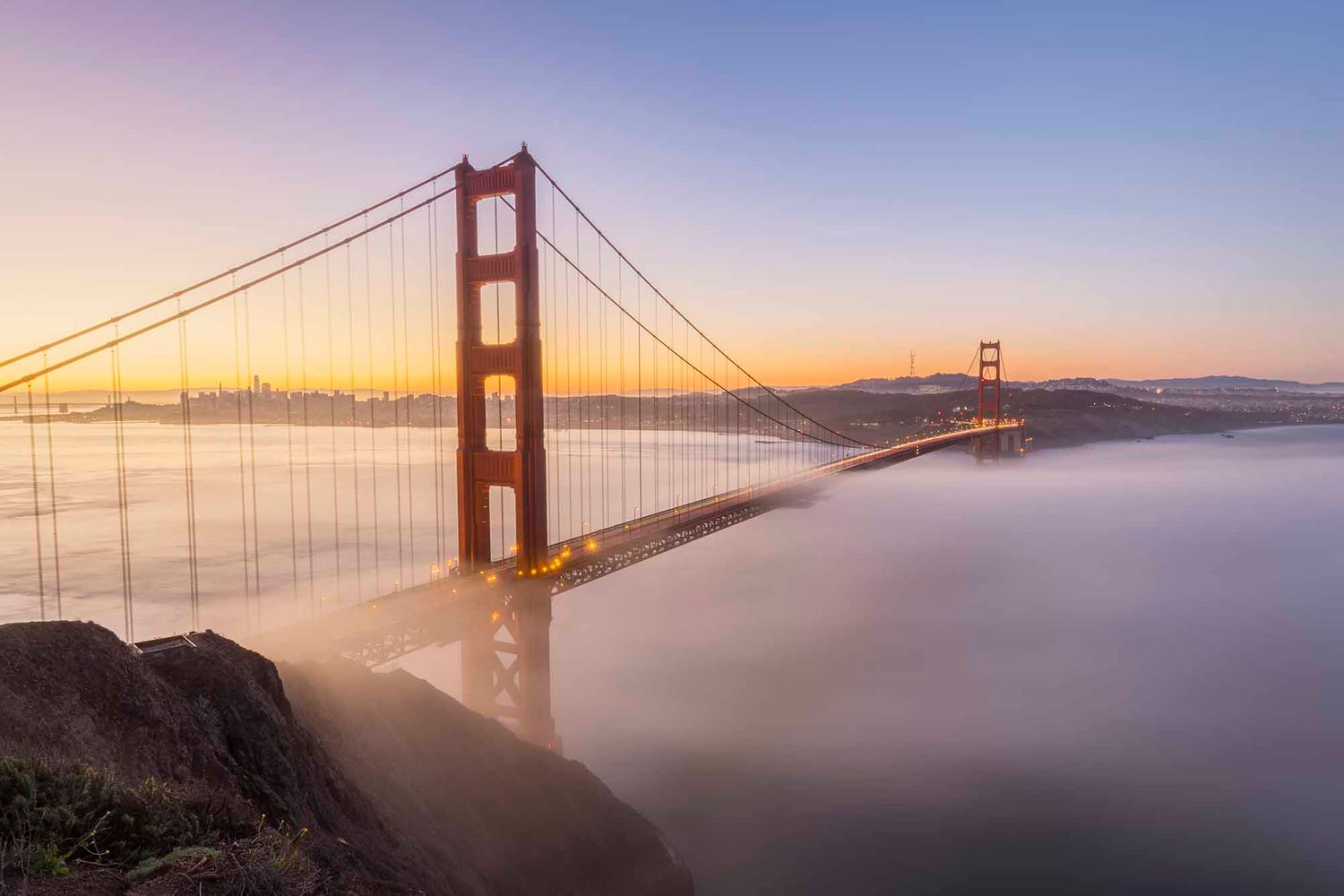 Golden Gate Bridge emerges from morning fog during sunrise in San Francisco Bay.