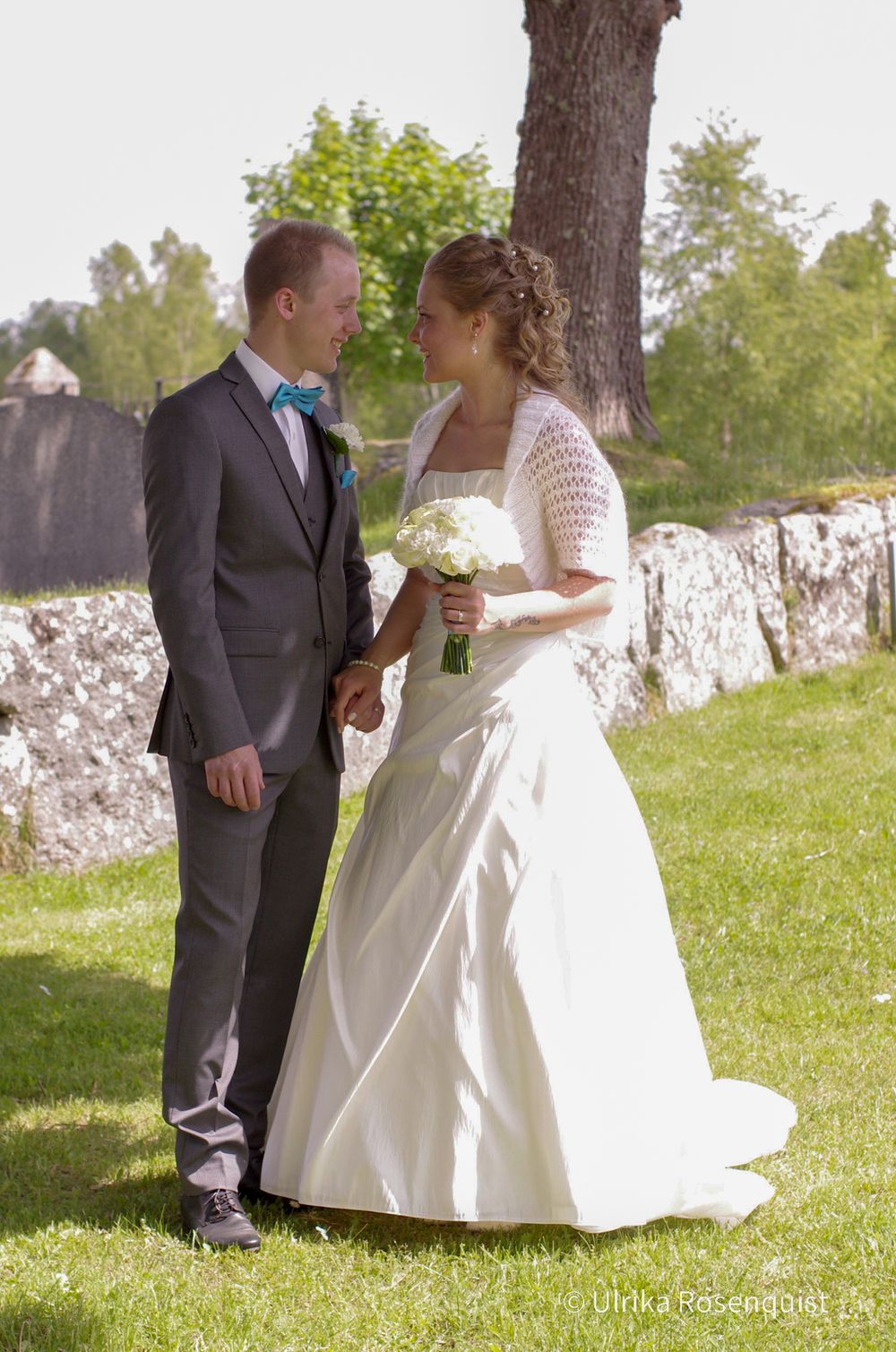 Newlyweds sharing intimate moment in garden setting near stone wall.