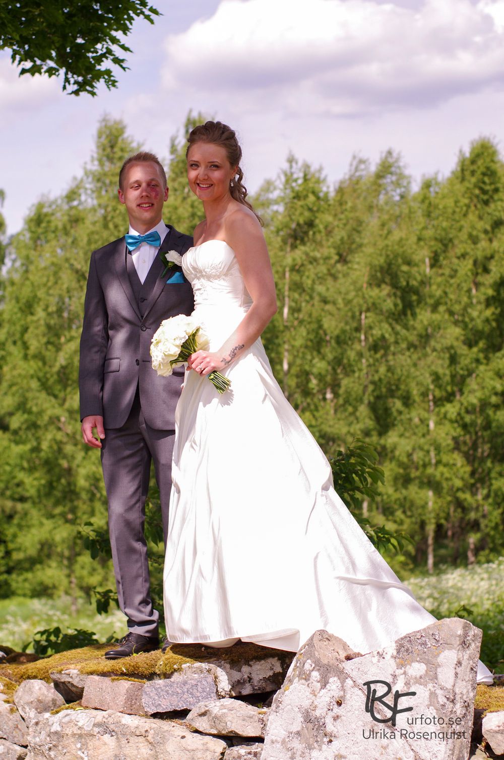 A newlywed couple posing on stone rocks surrounded by green trees.
