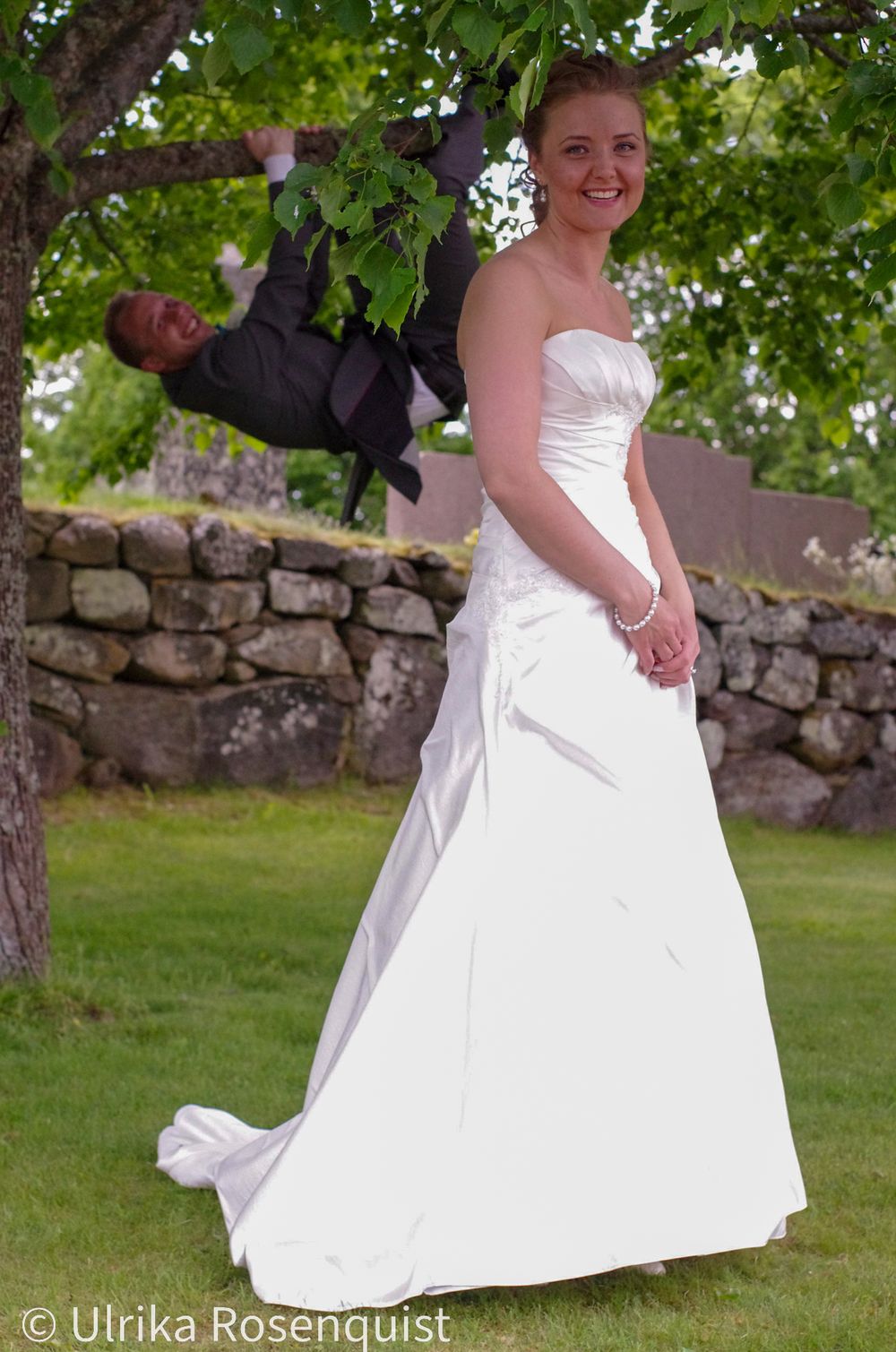 A whimsical wedding photo with playful poses near a stone wall and trees.