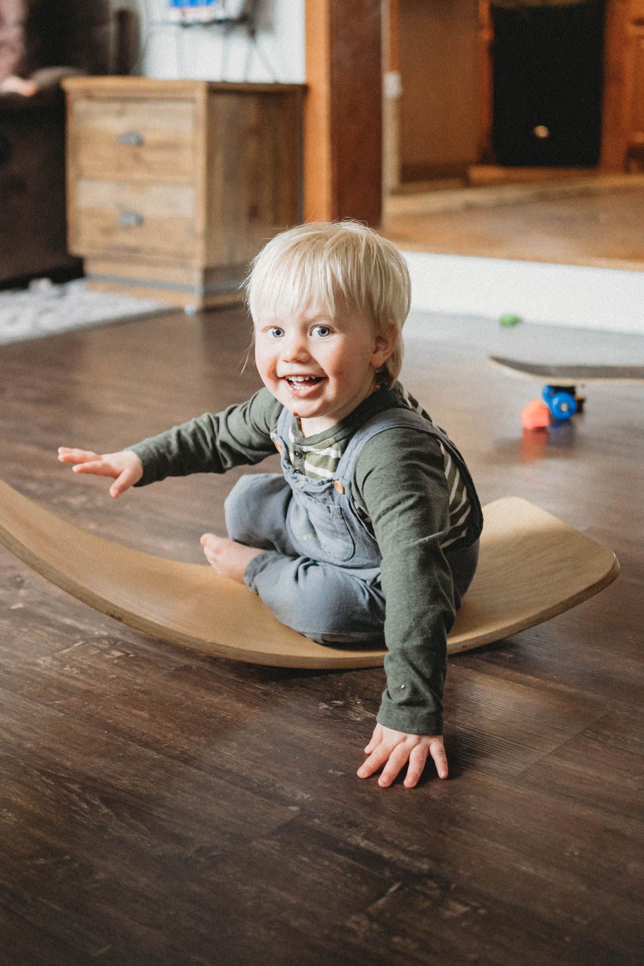 Child playing on wooden balance board in living room with hardwood floors.