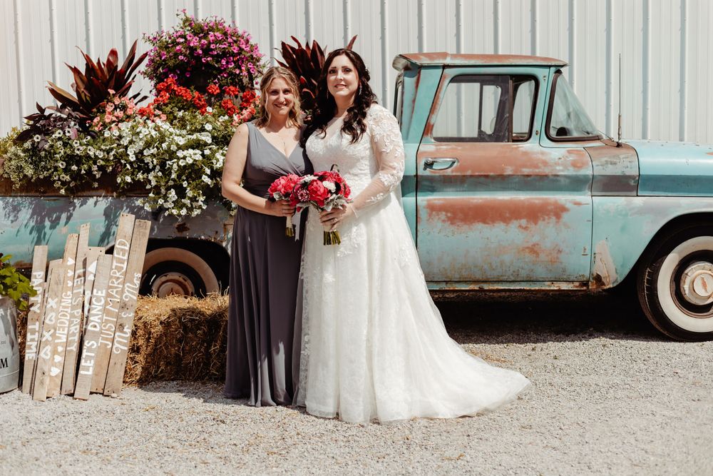 A rustic wedding photo featuring a vintage truck and floral decorations as backdrop.