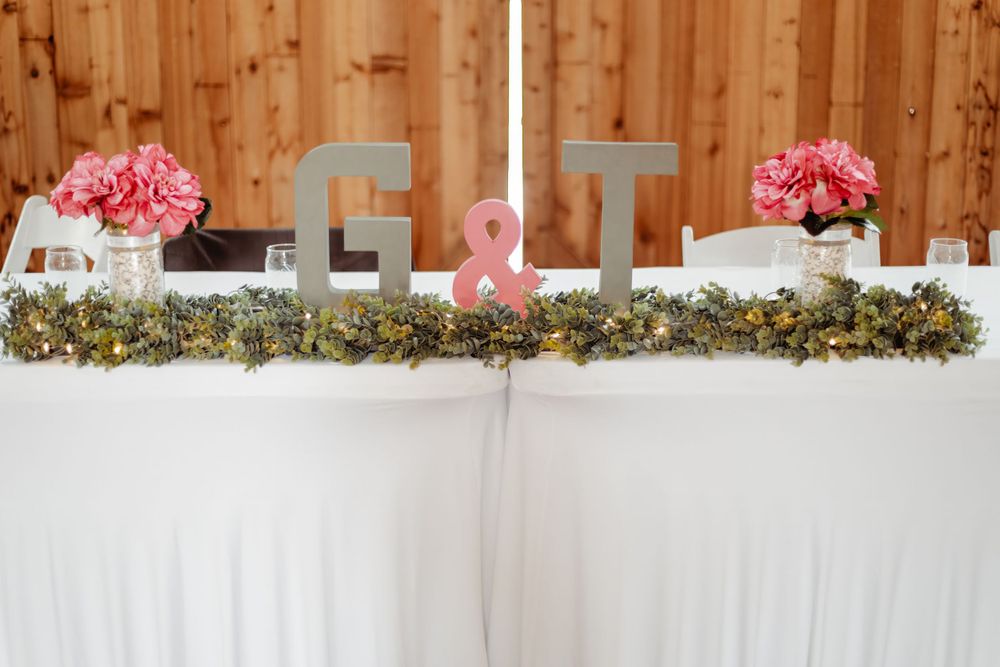 Wedding reception head table decor with pink flowers and initials on white tablecloth.
