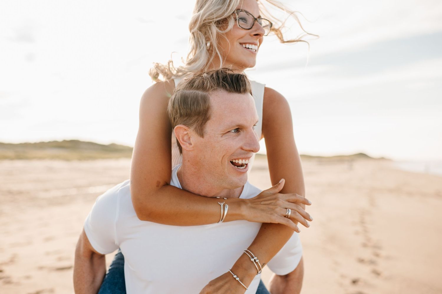 Joyful piggyback ride on sunny beach with wind-swept hair.