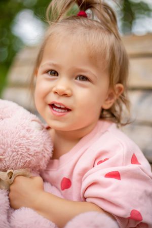 Pink heart-patterned clothing and plush toy create a sweet, cuddly moment.