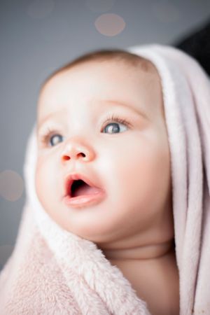 Close-up portrait wrapped in soft pink blanket with bokeh lights in background.