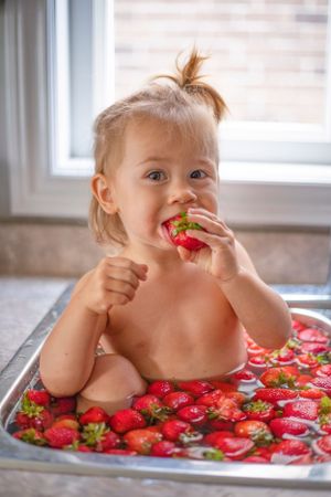 Joyful moment captured eating fresh strawberries in kitchen sink filled with bright red berries.
