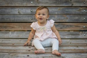 Baby portrait series on weathered wood background wearing light pink outfit.