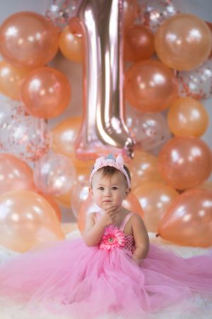 Baby's first birthday setup with pink tulle dress and peach balloon backdrop.
