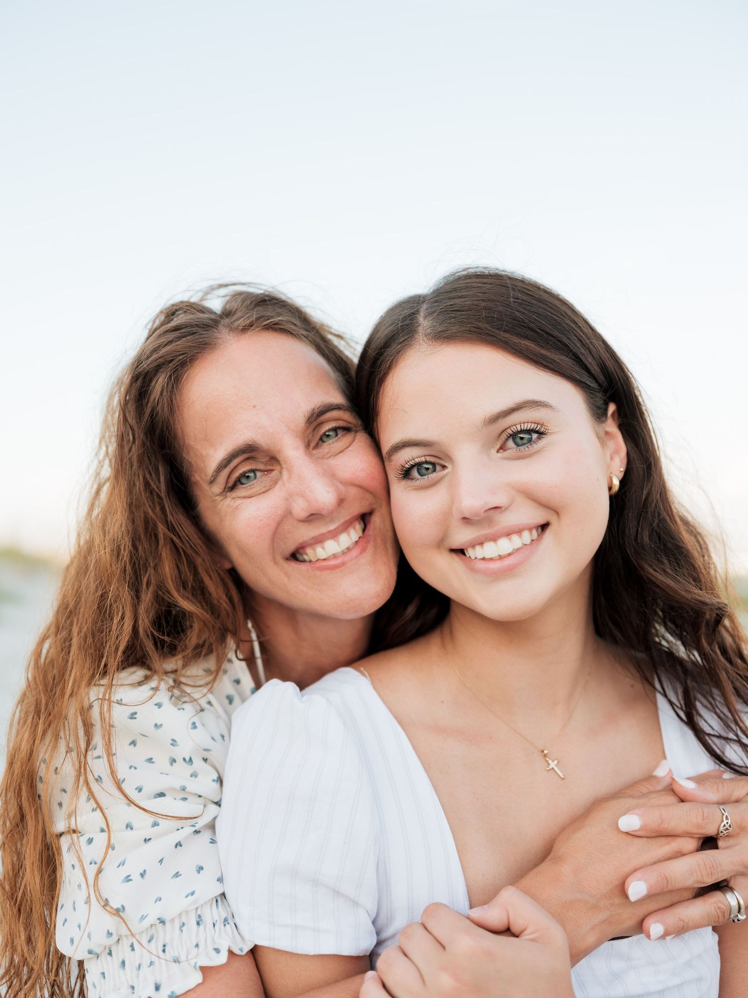 Two women with long dark hair sharing tender moment outdoors in white tops.