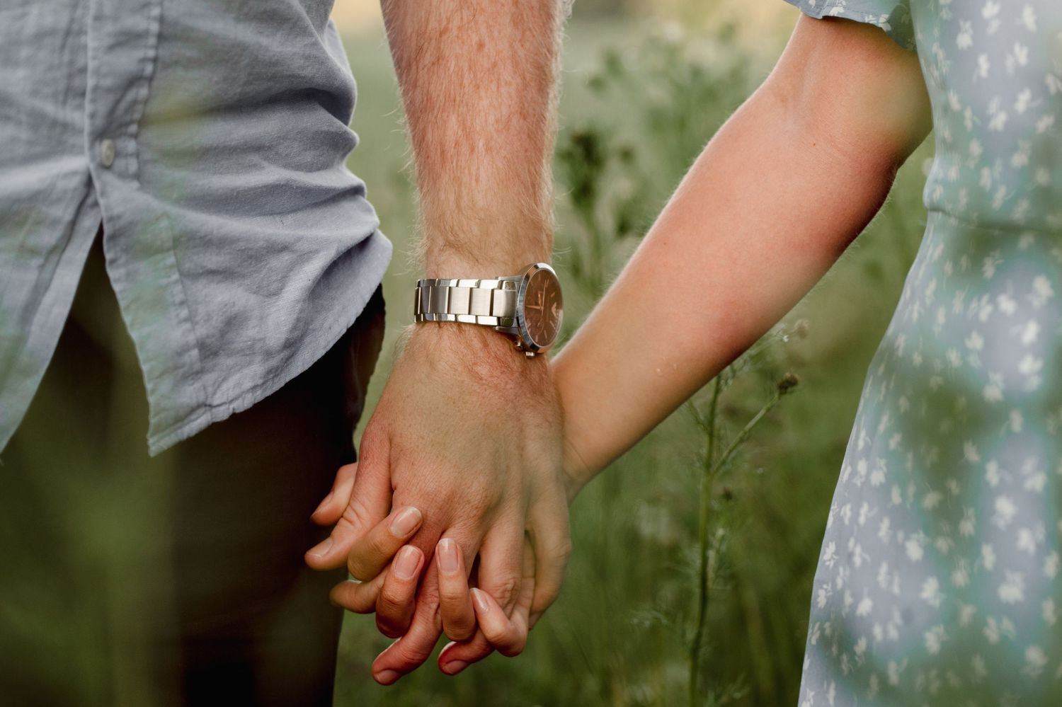 Close-up shot of two people holding hands with one wearing a silver watch.