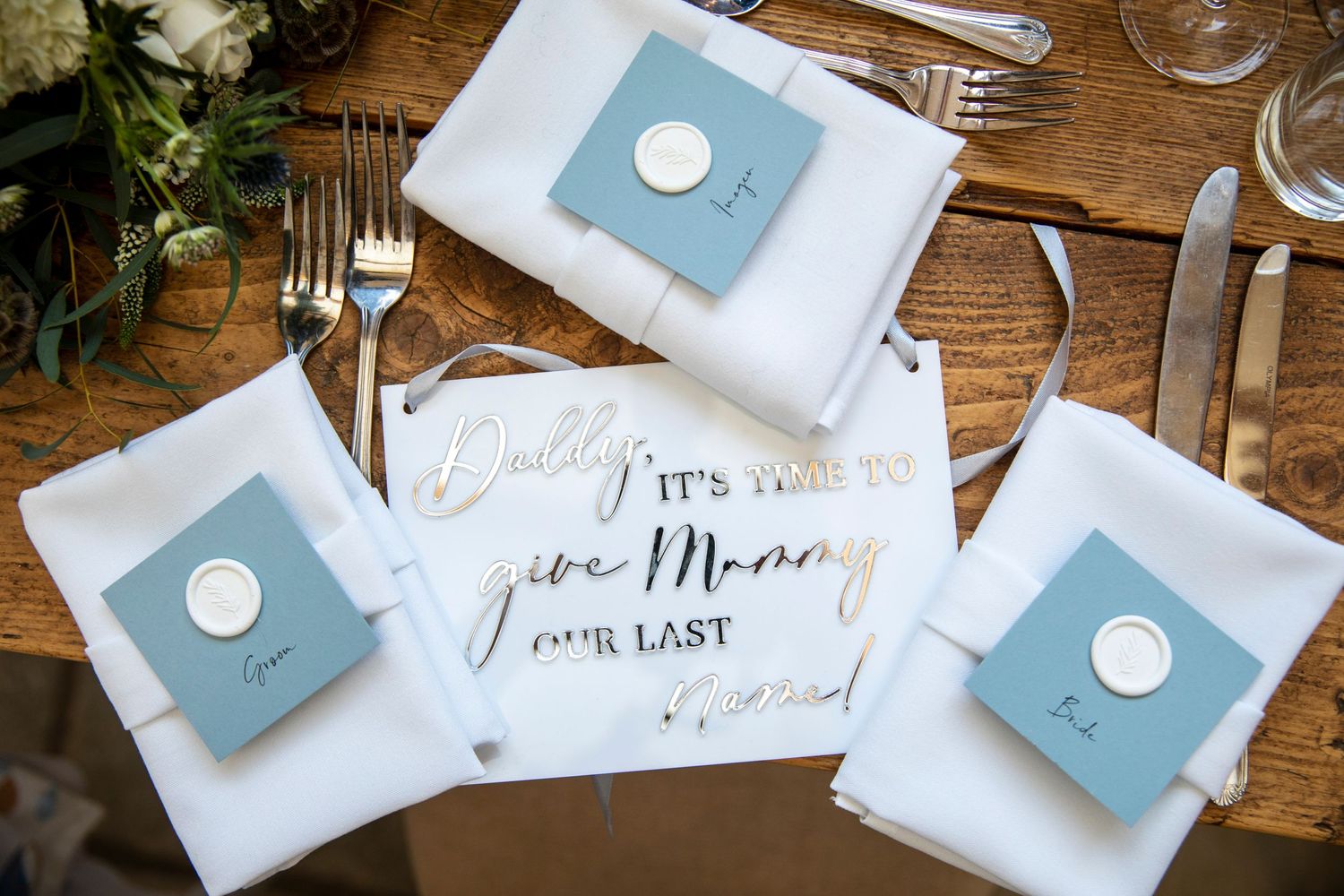 Elegant light blue and white wedding place cards and table settings arranged on a rustic wooden surface.