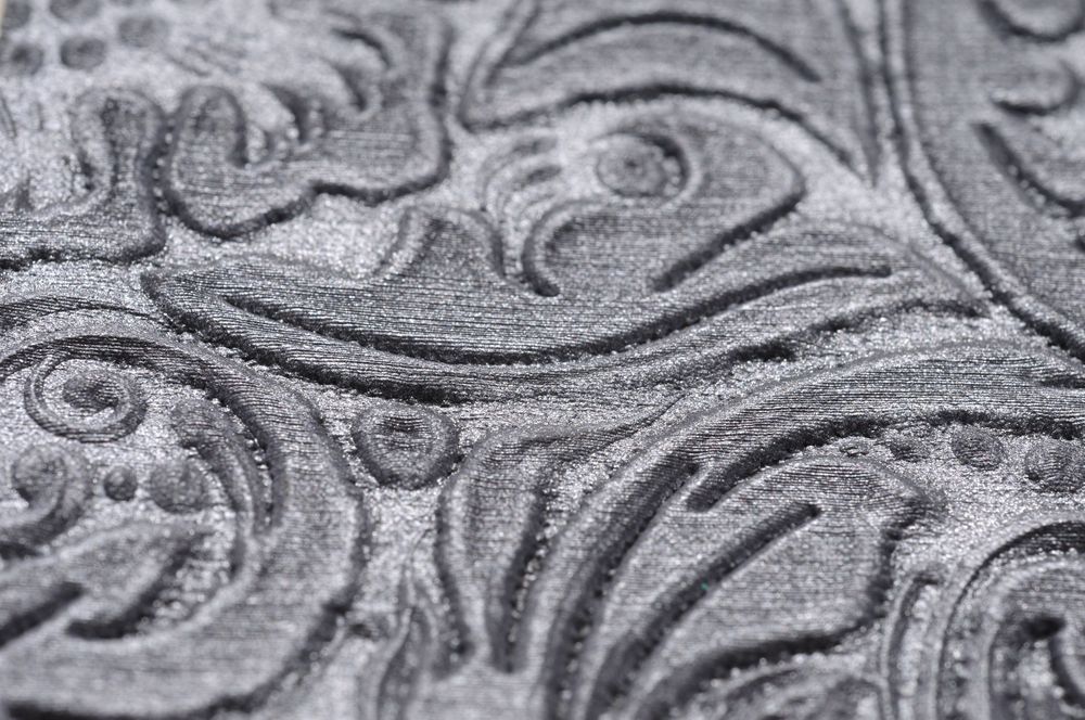 Extreme close-up macro photography of an embossed silver metal surface showing detailed swirling floral patterns.