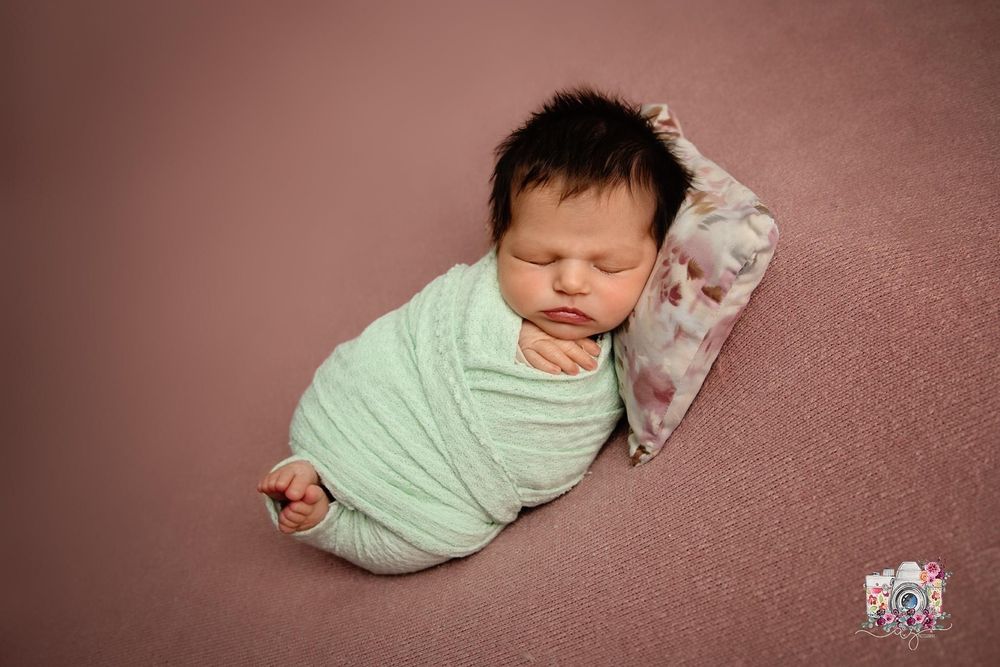 Peaceful newborn baby wrapped in mint green swaddle on pink backdrop.