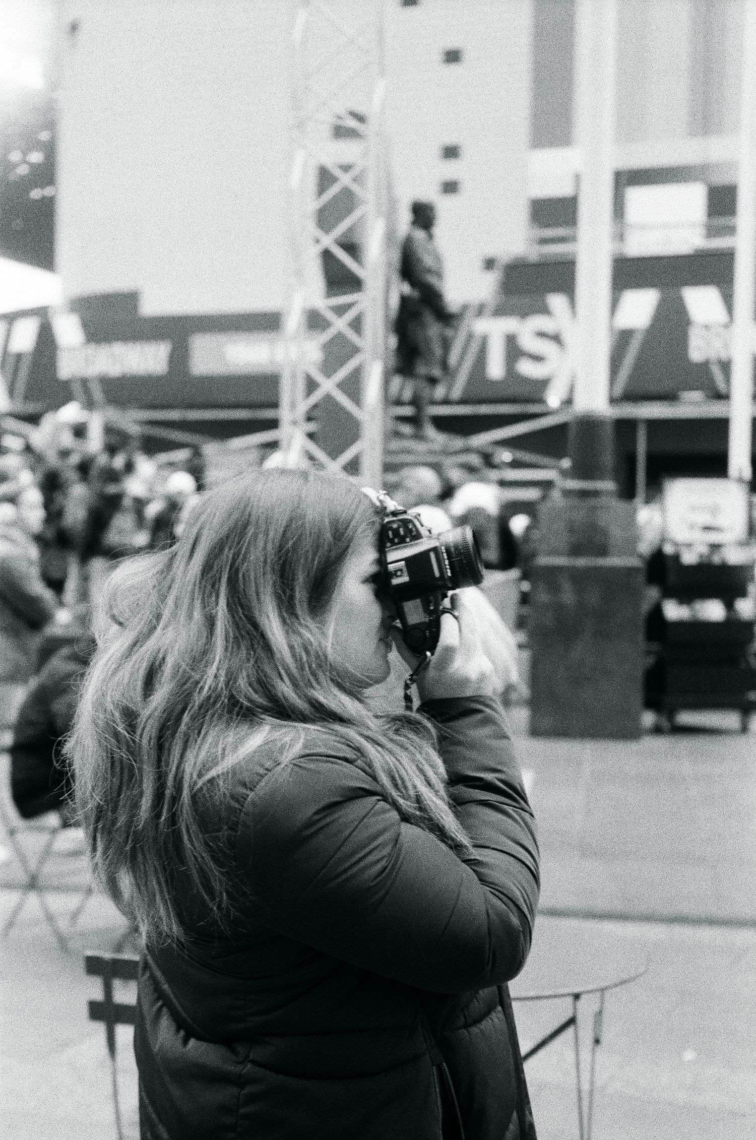 Black and white photo of a woman photographing an outdoor event with a film camera.