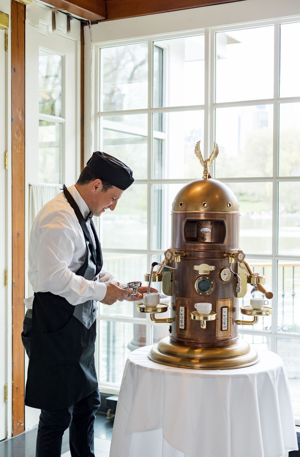 Server operates ornate brass coffee machine at elegant wedding reception.