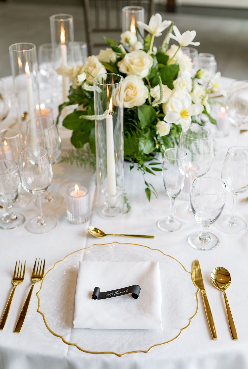 Formal wedding table setting with white roses centerpiece, gold rimmed plates and crystal stemware.