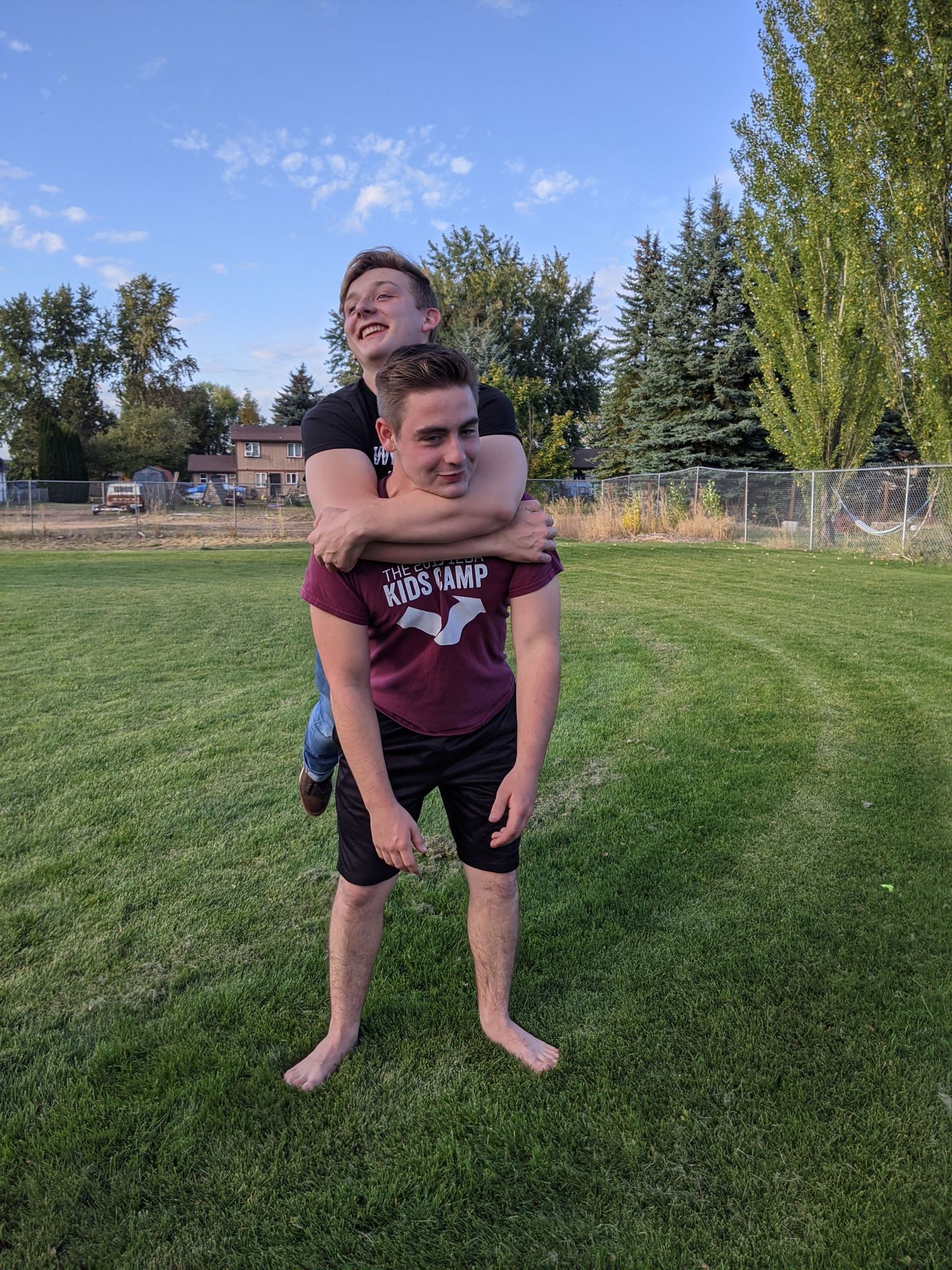 Friends sharing laughter during a piggyback ride on a sunny sports field.