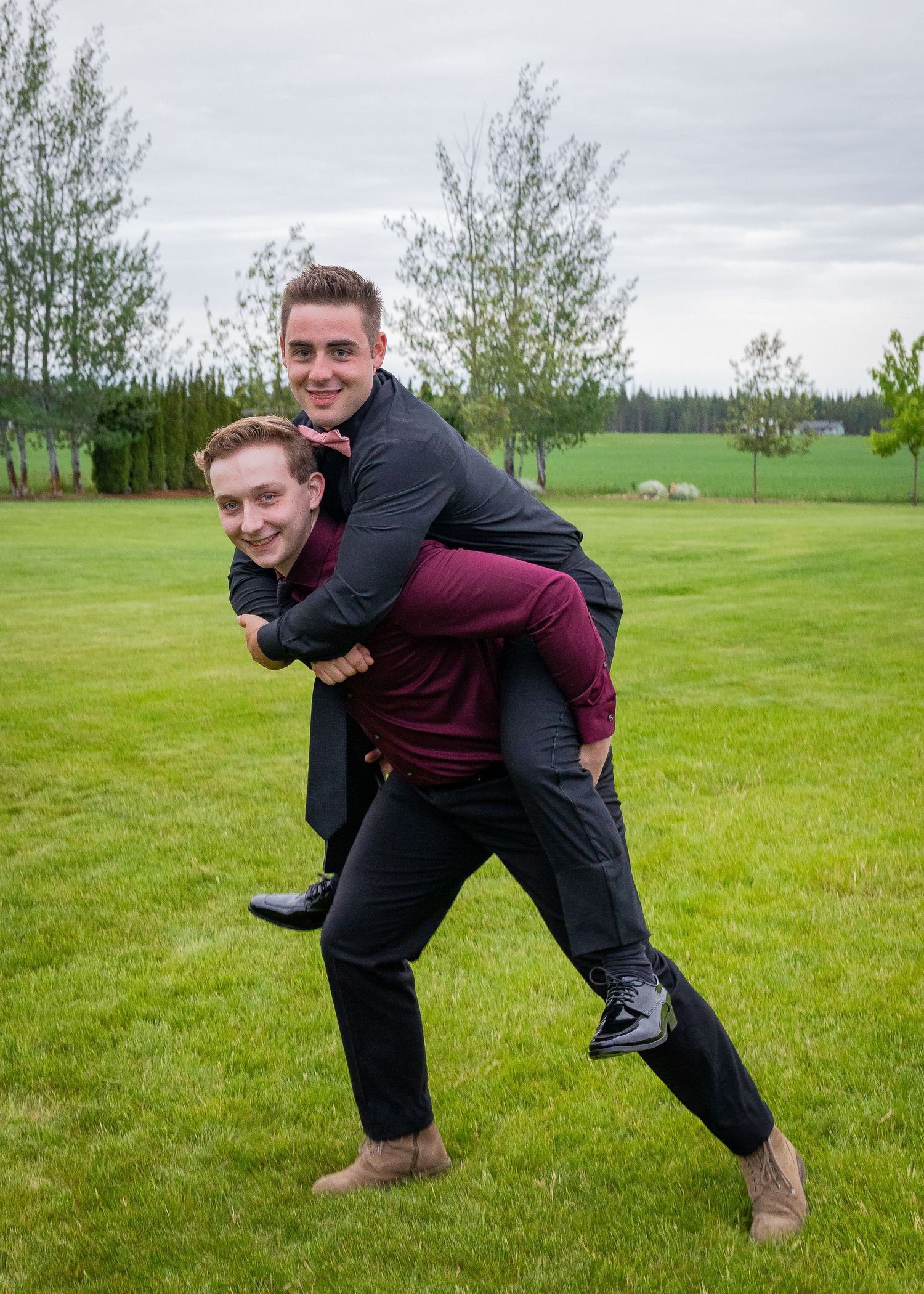 Two friends having fun with a piggyback ride on a green lawn with trees in background.