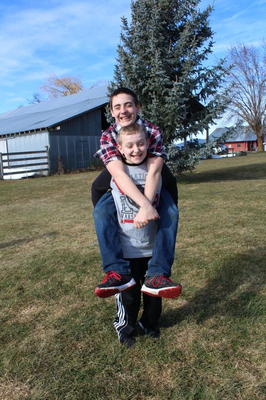 Playful piggyback ride captured in front of a barn and evergreen trees.