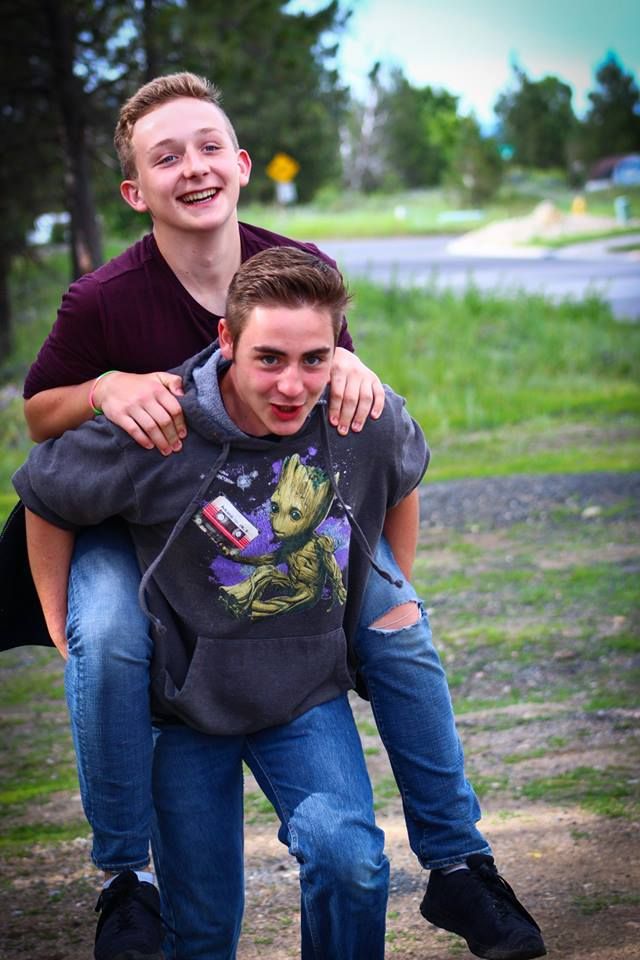 Friends share a fun piggyback ride moment on a path with trees in background.