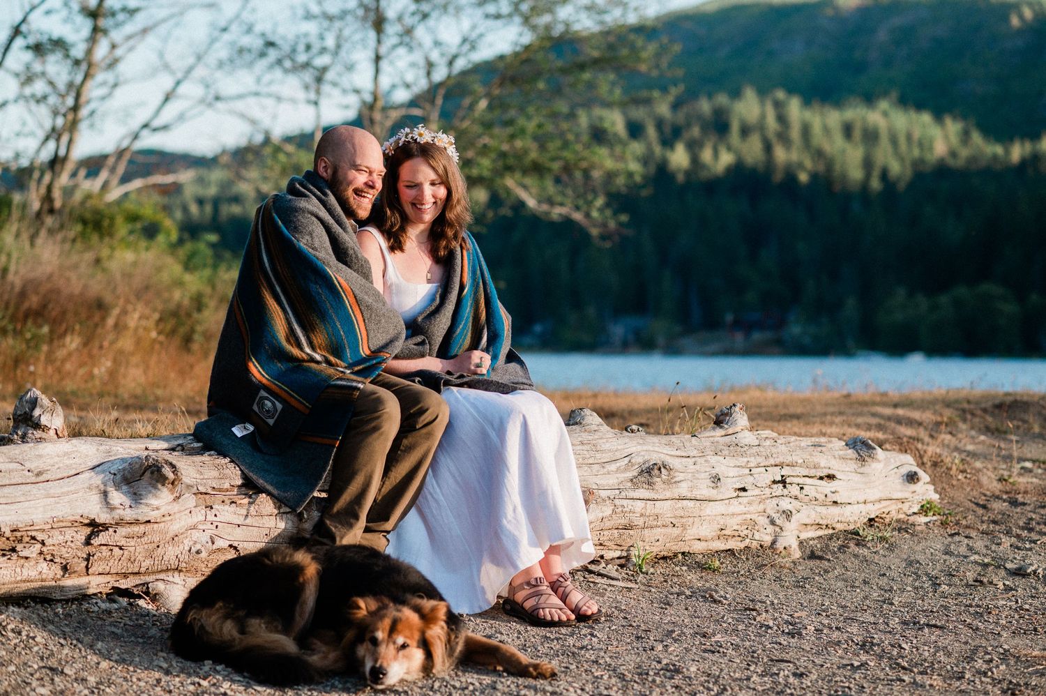 Bride and groom snuggle and laughing under blanket at Lake Crescent.