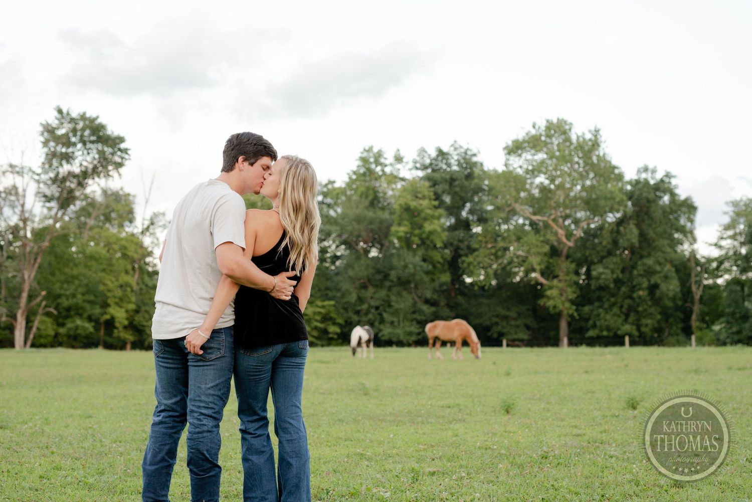 A romantic moment in a pasture with horses grazing in the background.