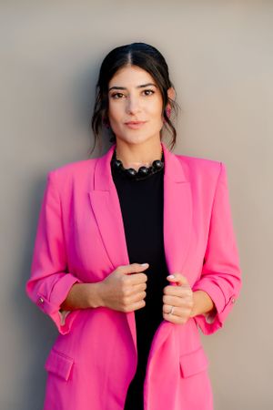 Woman wearing a bright pink blazer and black top poses confidently against neutral backdrop.