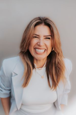 Portrait of a woman in light blue blazer with genuine laughter against gray backdrop.