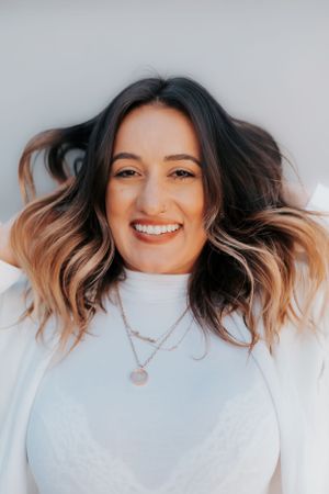 Portrait of a woman with wavy ombre hair wearing a white sweater and necklace.