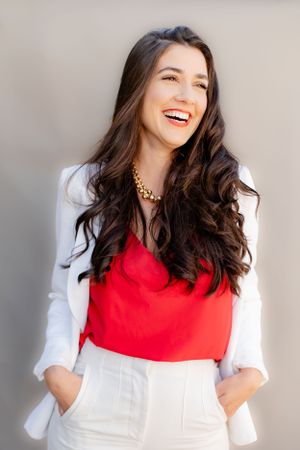 Professional portrait featuring a white blazer and red top with statement necklace.
