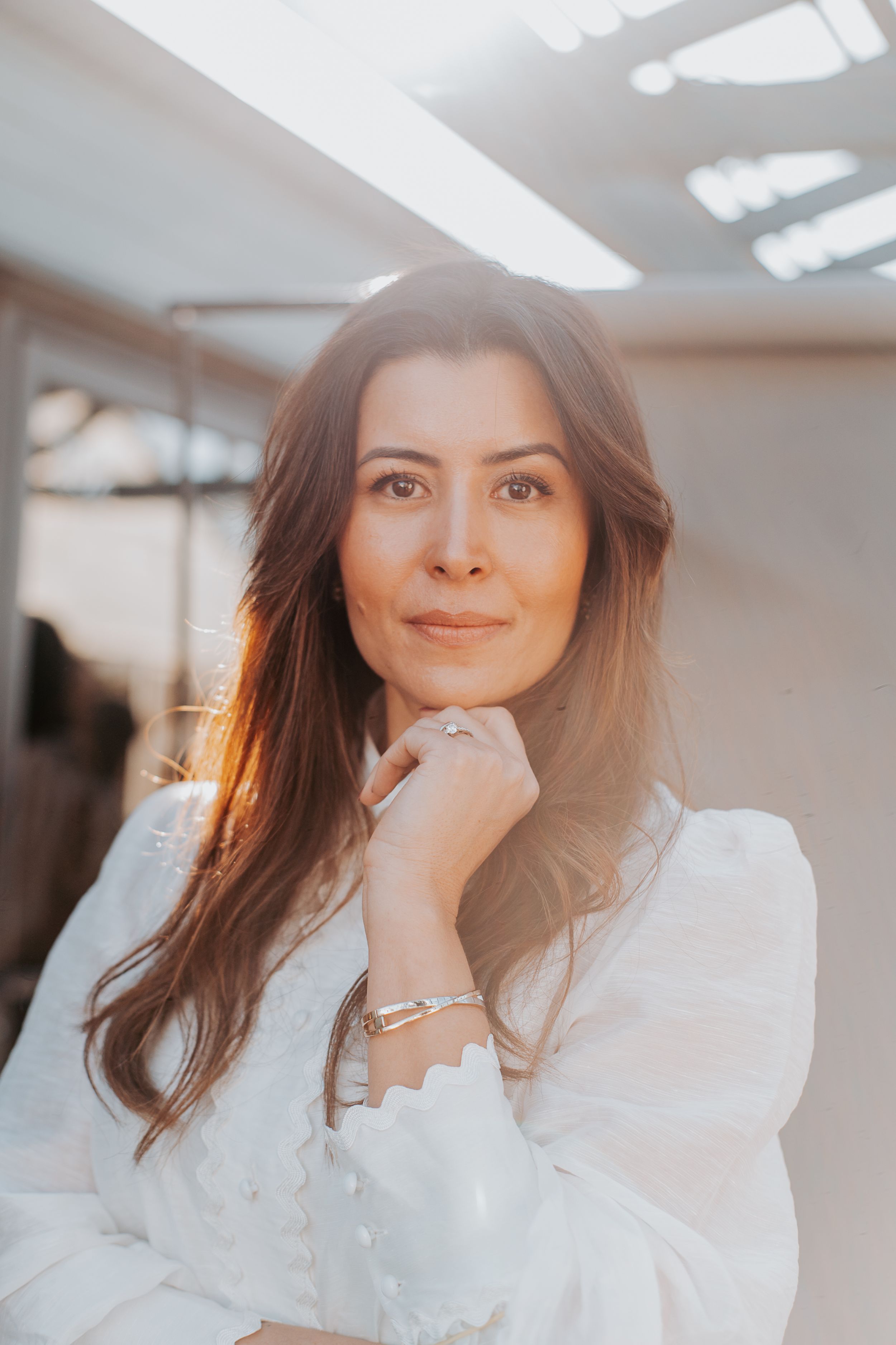 Warm-toned portrait of a woman in white blouse with soft lighting and elegant jewelry.