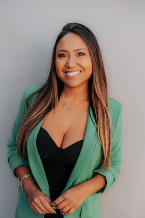 Professional portrait of a woman in a mint green blazer and black top against a gray background.