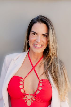 Woman in a white blazer and red swimsuit poses for a professional headshot.