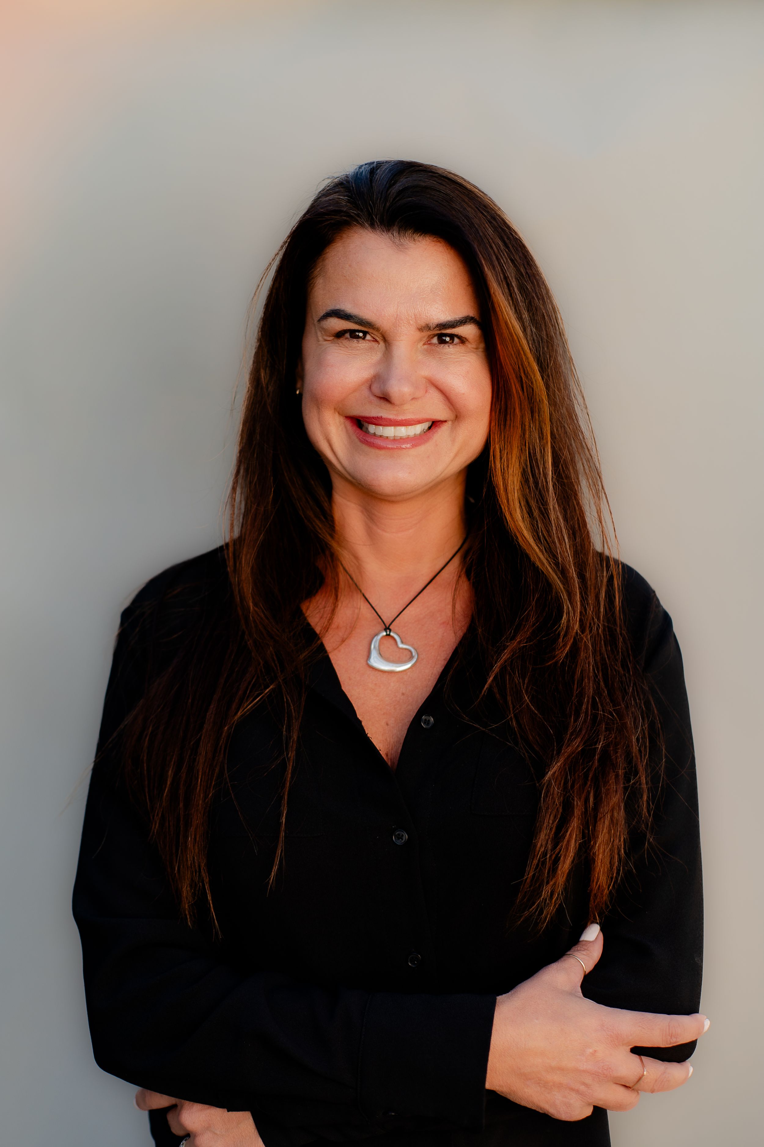 Professional headshot of a woman in black wearing a pendant necklace against neutral background.