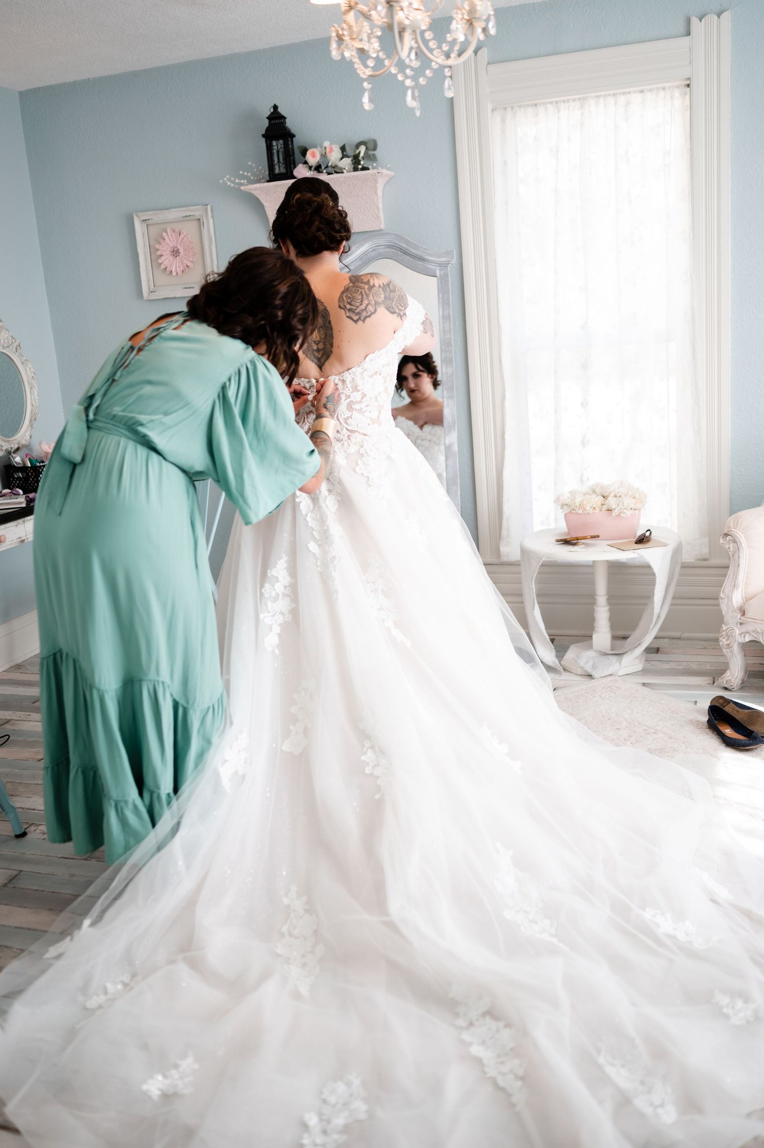 Behind-the-scenes moment of wedding dress preparation in an elegant powder blue room with chandelier.