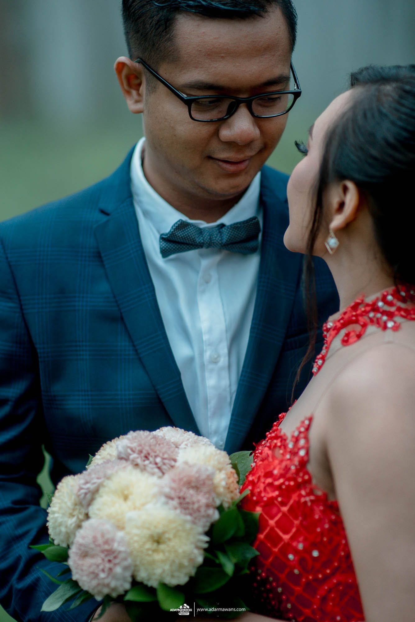 Close-up shot of couple with bouquet, bride in red dress and groom in navy suit with bow tie.