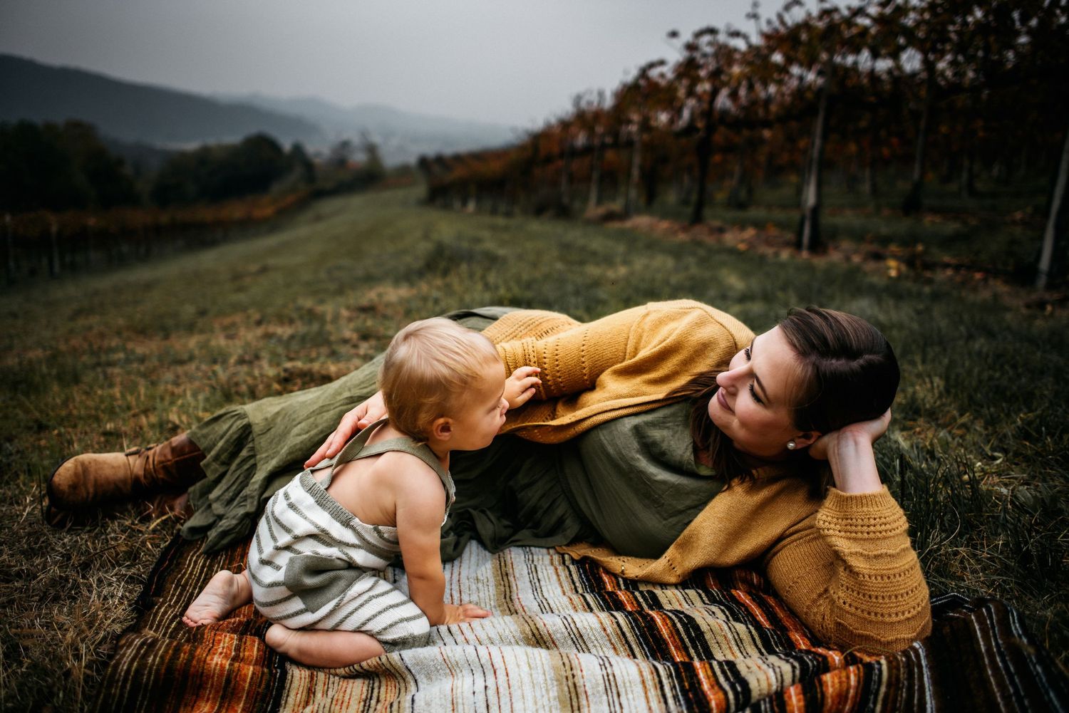 Mother and son laying on a blanket looking at each other in a vineyard in Vicenza, Italy.