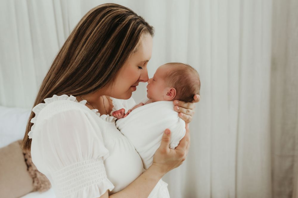 Intimate portrait of tender bonding moment between parent and newborn in white clothing.