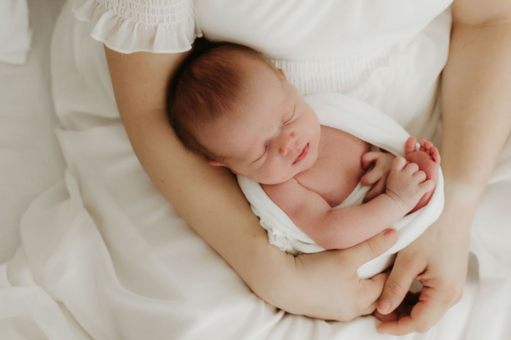 Sleeping newborn baby resting peacefully on parent's arms against white fabric.