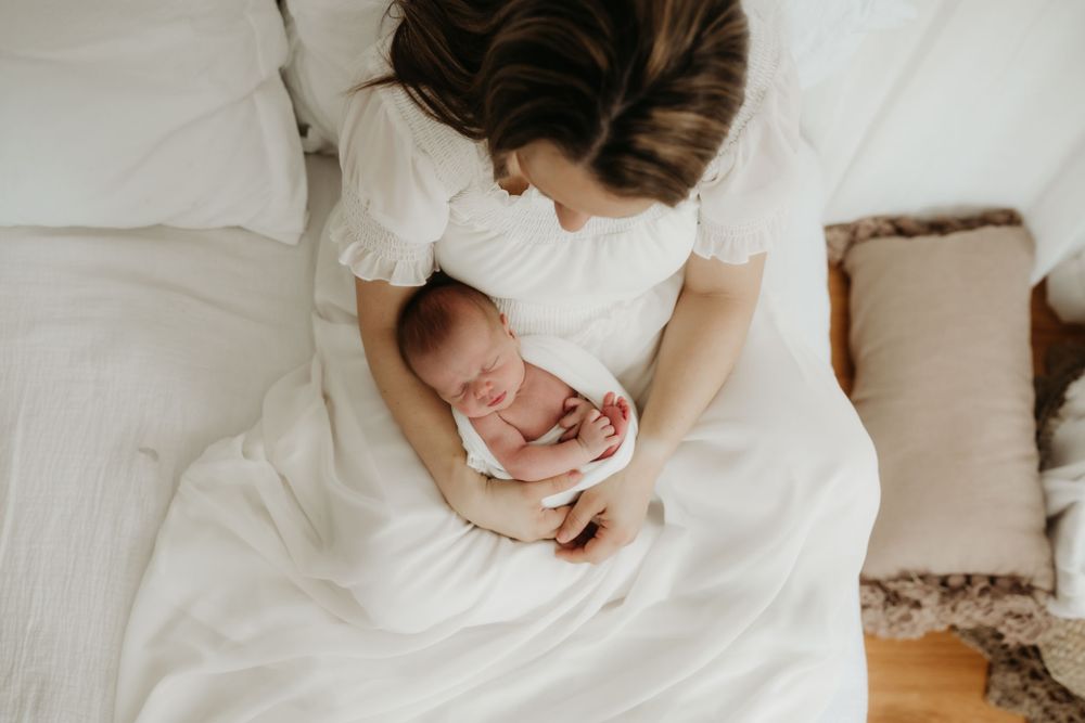 Overhead view of parent cradling sleeping newborn on white bedding.