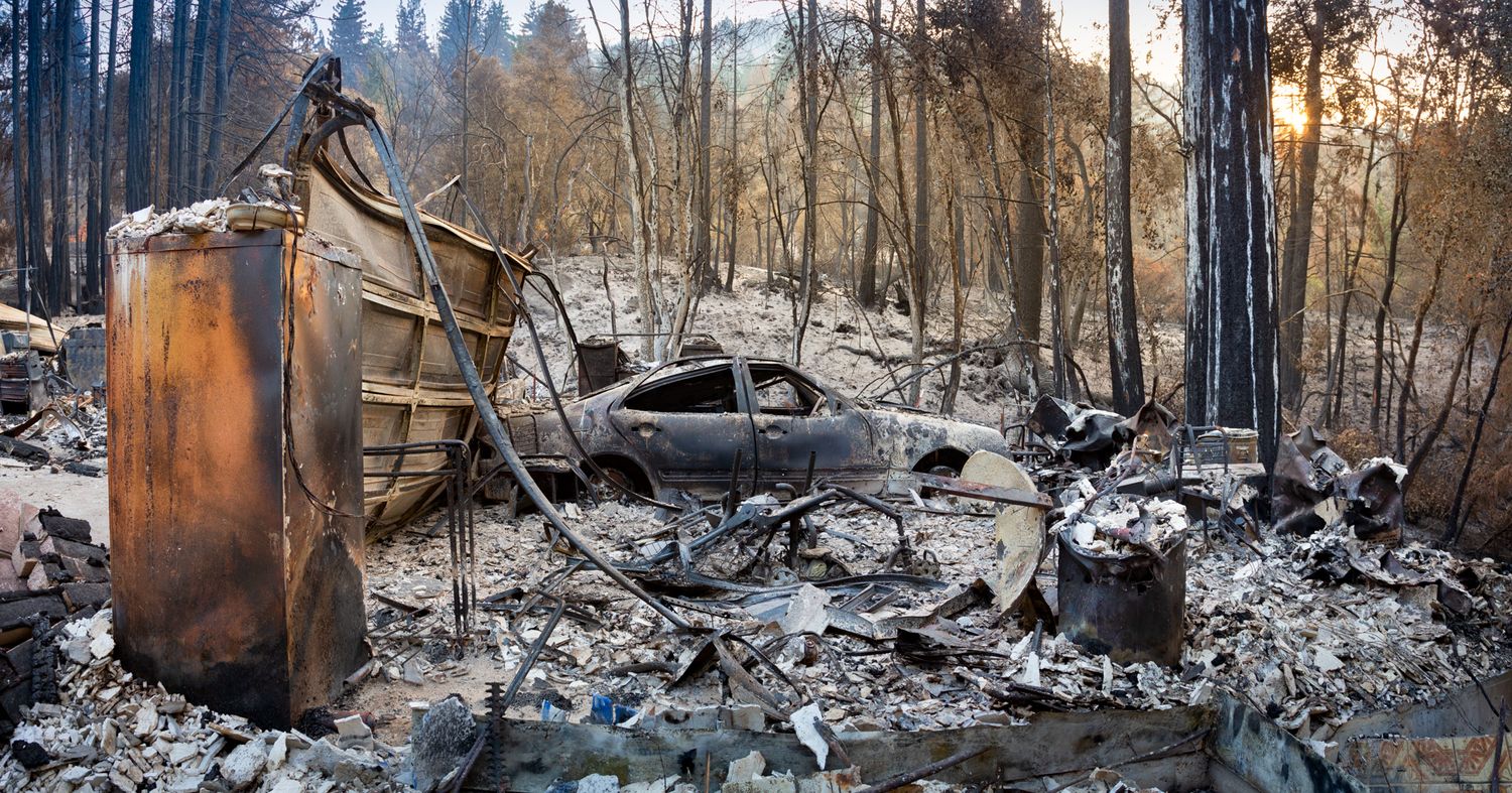 Burnt remains of a destroyed structure and vehicle after a devastating forest fire.