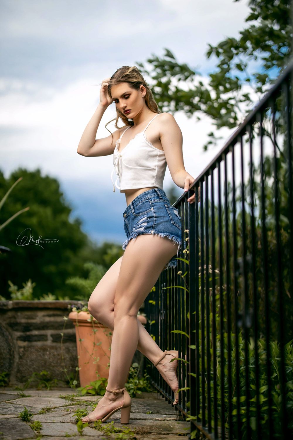 Stylish summer portrait against iron railing with cloudy sky background.