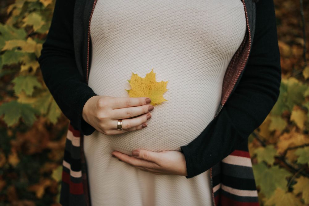 mama przykłada jesienny liść do ciążowego brzuszka - fotograf Kraków