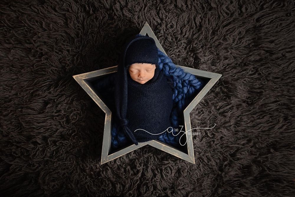 Professional newborn portrait with star-shaped prop and navy swaddle on brown textured background.