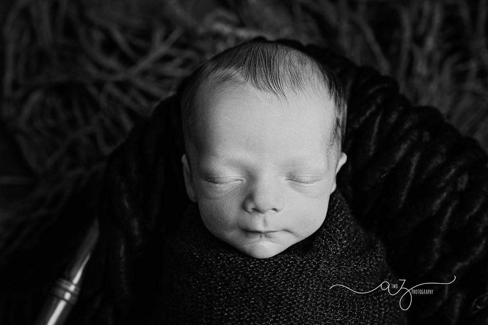 Black and white portrait of sleeping newborn in dark wrap with artistic lighting.